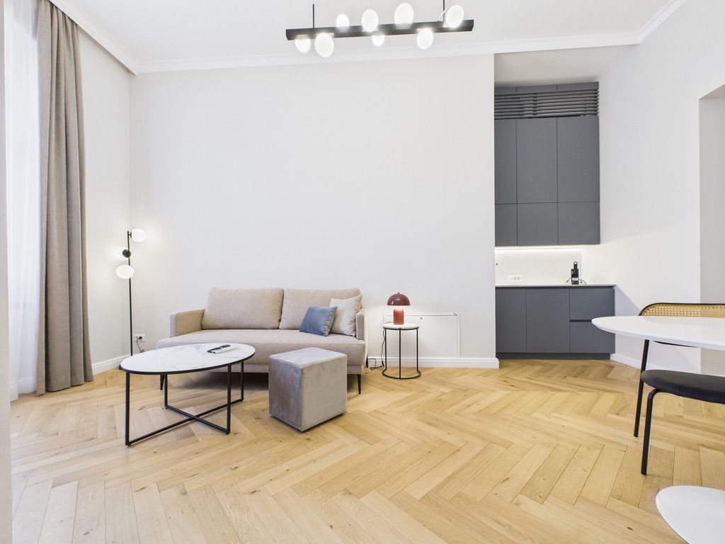 Un salon moderne comprenant un canapé, un pouf et une table basse, un coin cuisine avec des placards et une table à manger.
