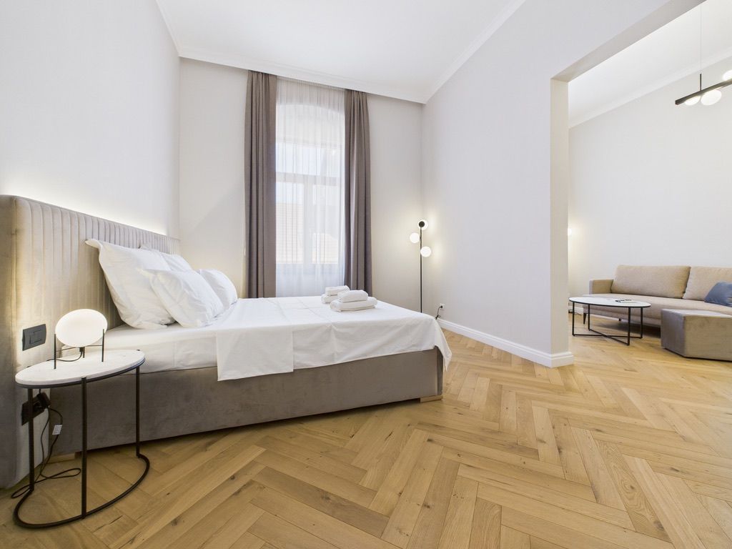 Una habitación de hotel moderna con una cama, una mesita de noche y un sofá en la zona de estar contigua.