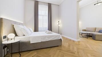 Una habitación de hotel moderna con una cama, una mesita de noche y un sofá en la zona de estar contigua.