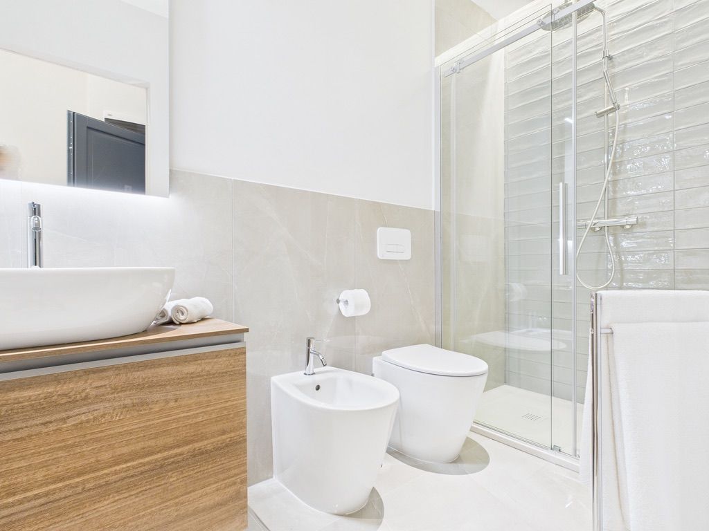 Un bagno moderno con un lavandino ampio, due bidet, un water e uno spazio doccia con pareti in vetro.