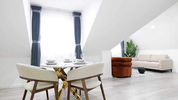 A modern dining area with a round table, two chairs, and a sofa in a bright living space. - The Wembley Crown Heights 1 Bed Flat  (Wembley)