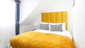 A hotel room with a bed, a nightstand, a lamp, and a window with curtains. - The Wembley Crown Heights 1 Bed Flat  (Wembley)