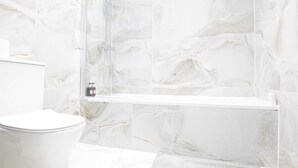A bathroom with a marble wall, a white toilet, and a shower enclosure. - The Wembley Crown Heights 1 Bed Flat  (Wembley)
