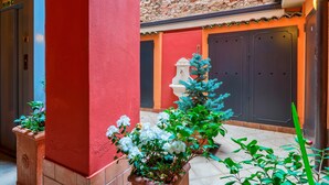 A courtyard with a red wall, a tiled floor, a white column, and a blue tree. - Laura's Home (Brescia)