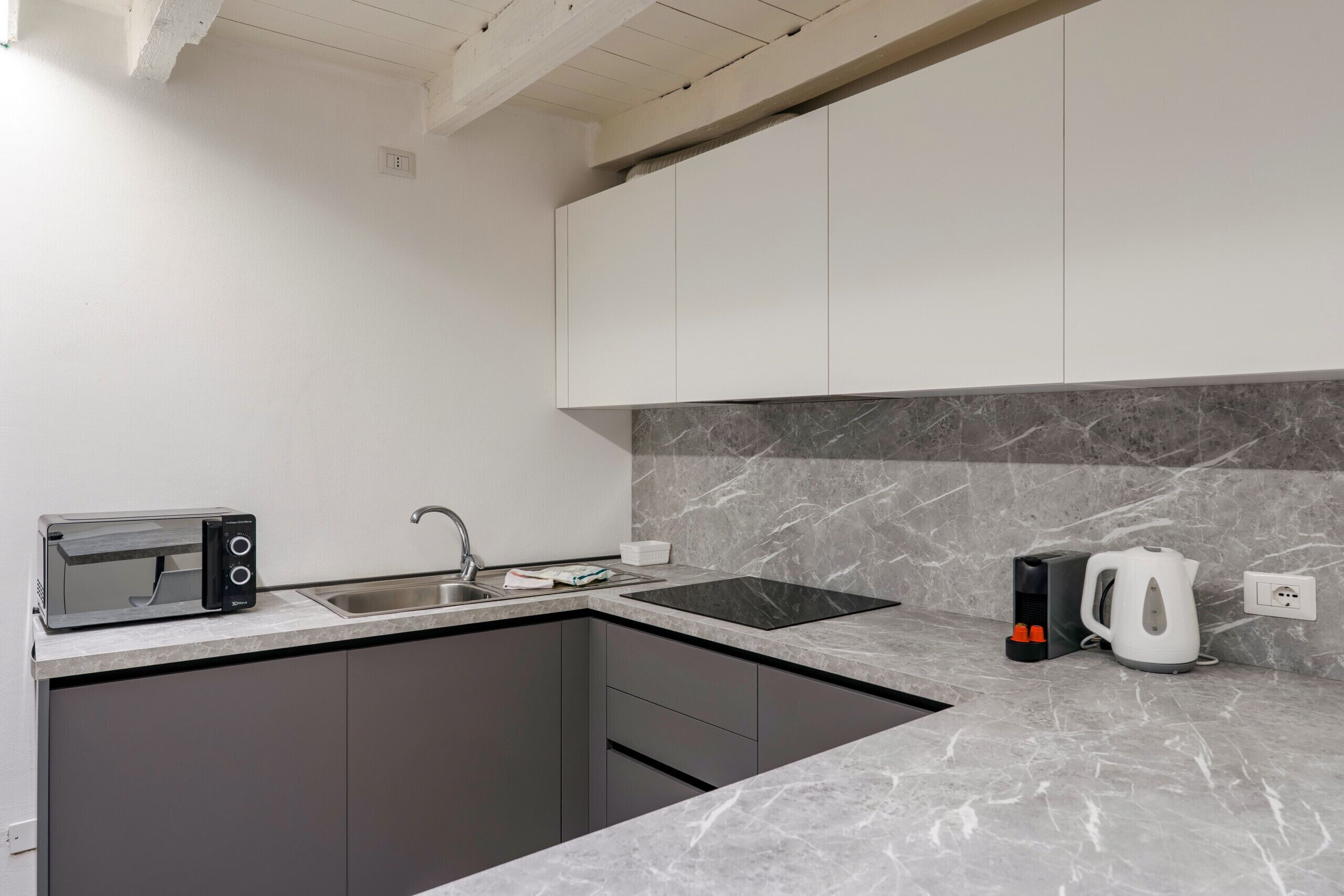 A modern kitchen with a built-in microwave, sink, and kettle.