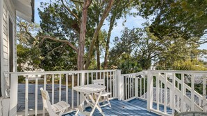 A blue wooden deck with white railings, a white folding chair, and a small round table.
