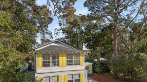 A two-story building with a gabled roof, large windows with yellow shutters, and a gravel driveway.
