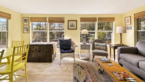 A room with a dining table, chairs, a sofa, a coffee table, a lamp, and a window with a view.