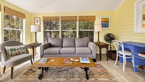 A living room with a sofa, armchairs, a coffee table, a desk, and a fan.