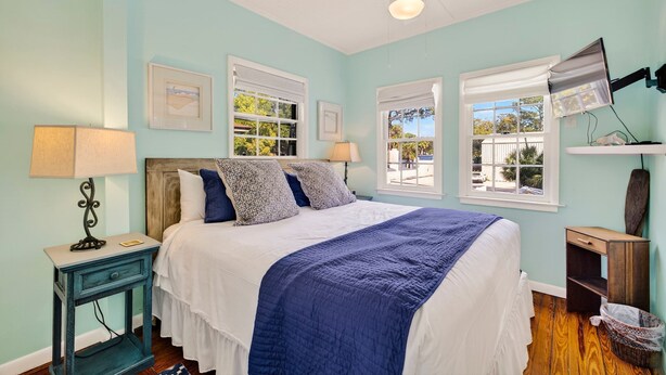 A bedroom with a bed, two bedside tables, a ceiling fan, and a window with a view.