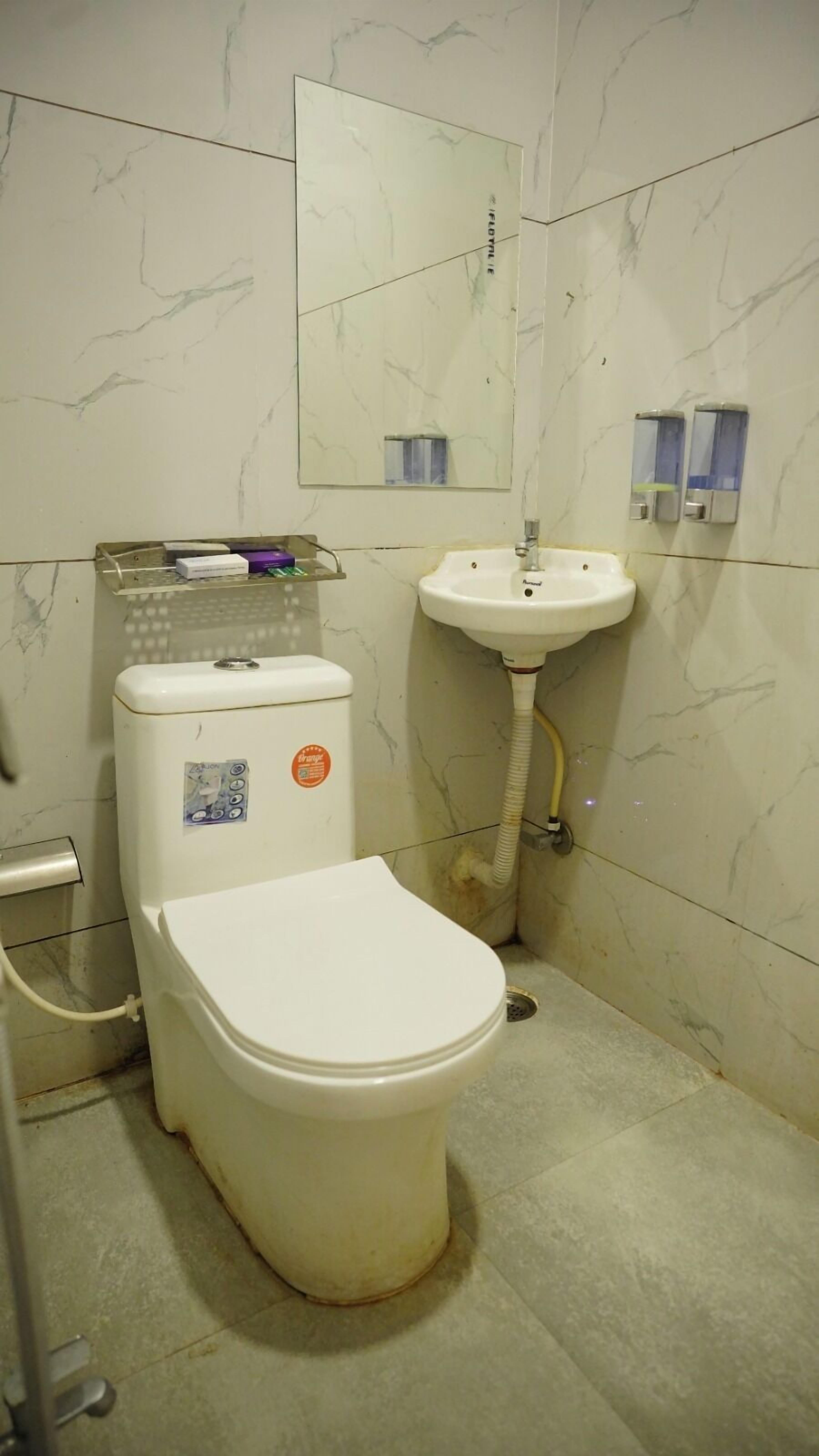 Une salle de bain équipée d’un WC, d’un lavabo, d’un miroir et d’un distributeur de savon.