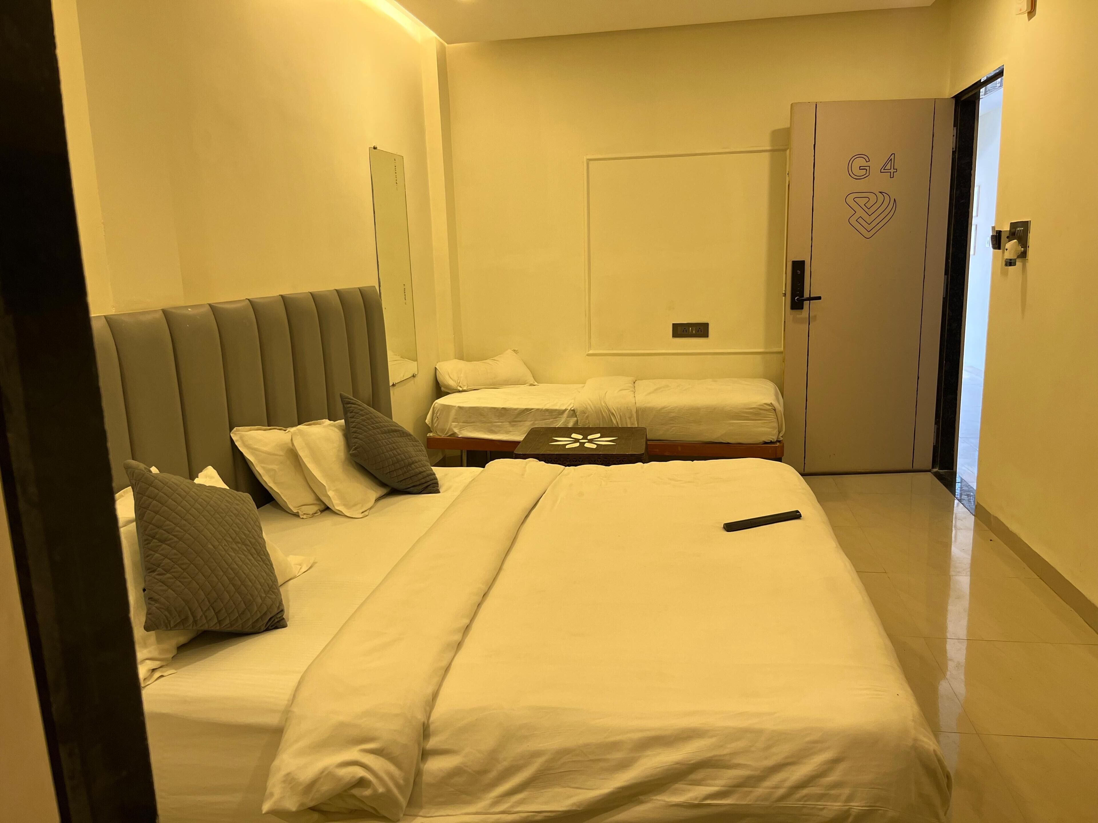 A hotel room with a large bed, a smaller bed, a bedside table, a mirror, a wardrobe, and a door.