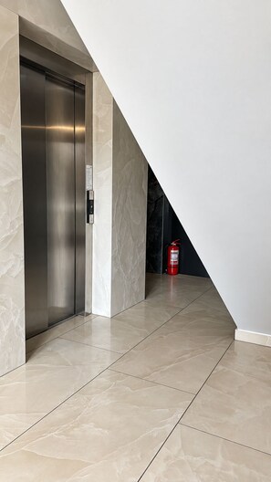 An interior space with a metallic elevator, a fire extinguisher, and a tiled floor. - MaisonA (Timișoara)