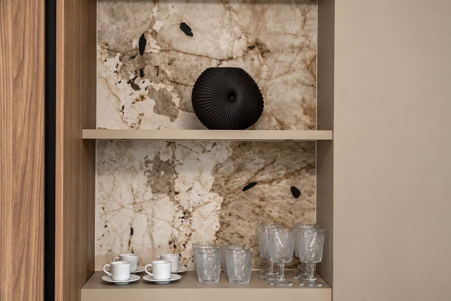 A shelf with a marble wall background, a black decorative item, and a set of white cups and glasses.