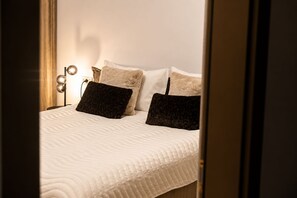 A neatly made bed with a white quilt, two dark pillows, and a bedside lamp with multiple bulbs. - MaisonA (Timișoara)