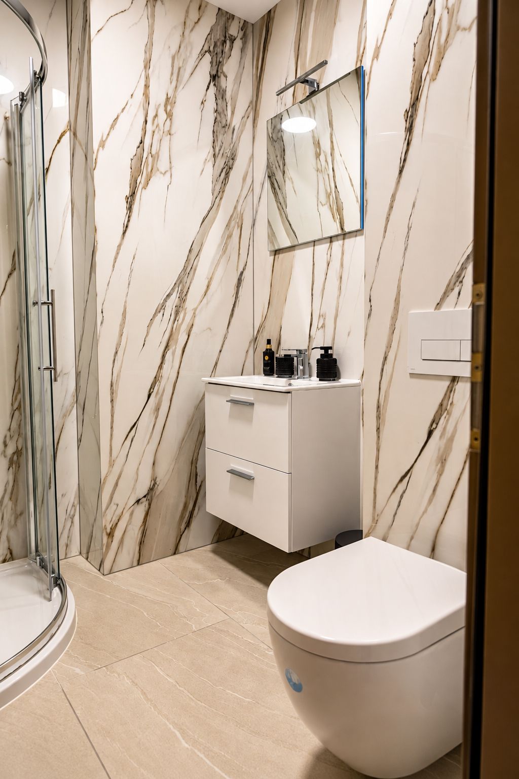 Un baño con pared de mármol, cabina de ducha de vidrio, lavamanos blanco y un inodoro.