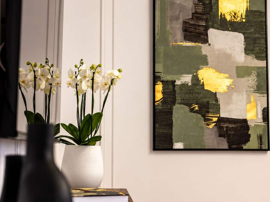Una habitación con una mesa de madera, un jarrón blanco con flores blancas y un cuadro abstracto enmarcado en la pared.
