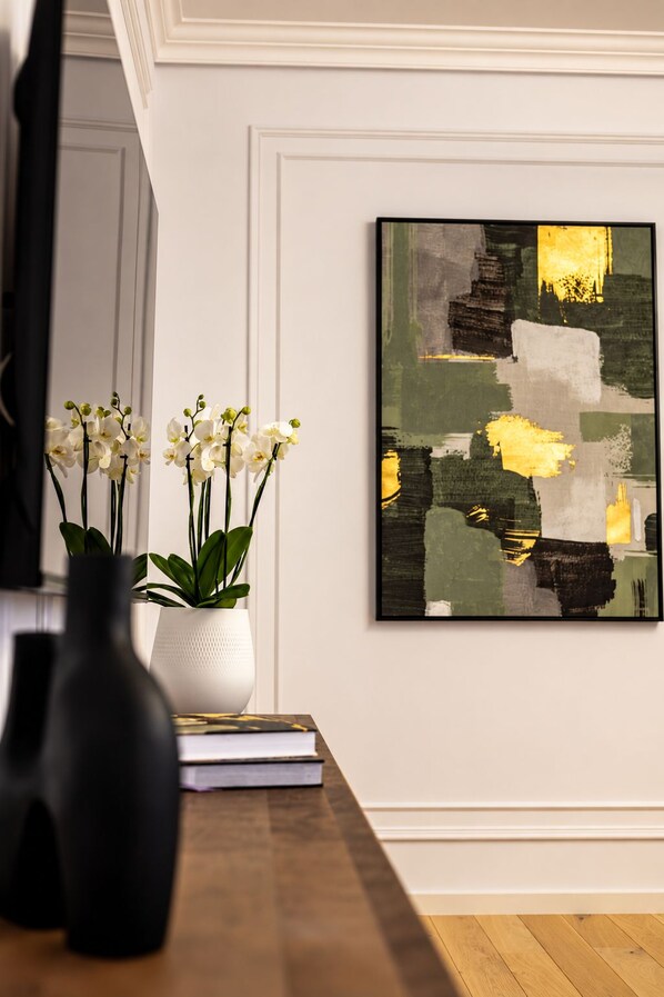 A room with a wooden table, a white vase with white flowers, and a framed abstract painting on the wall. - MaisonA (Timișoara)