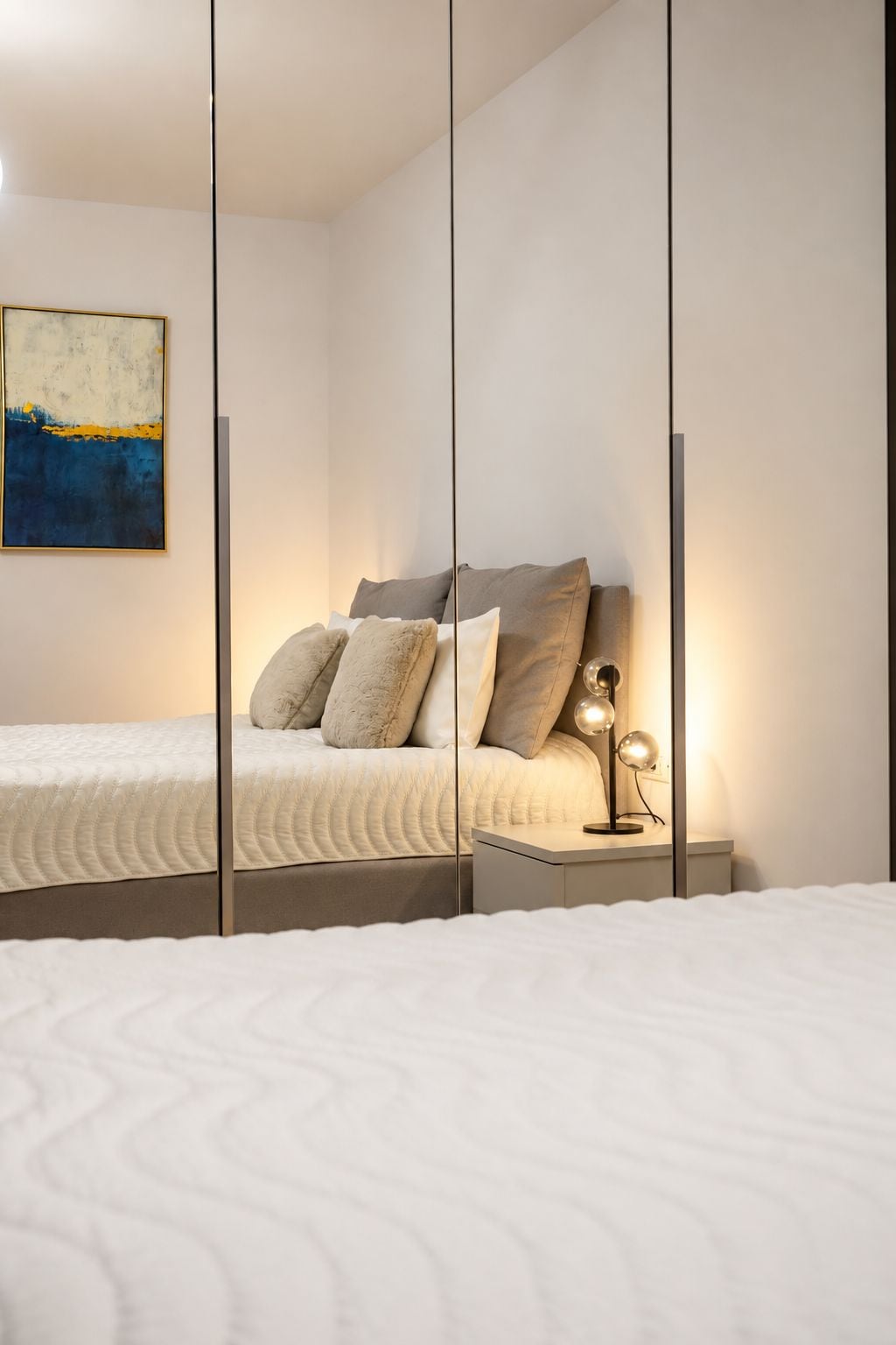 Une chambre à coucher moderne avec un lit, des oreillers, une lampe de chevet et un tableau accroché au mur.