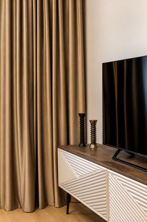 A room with a television on a wooden cabinet, beige curtains, and a patterned cabinet. - MaisonA (Timișoara)