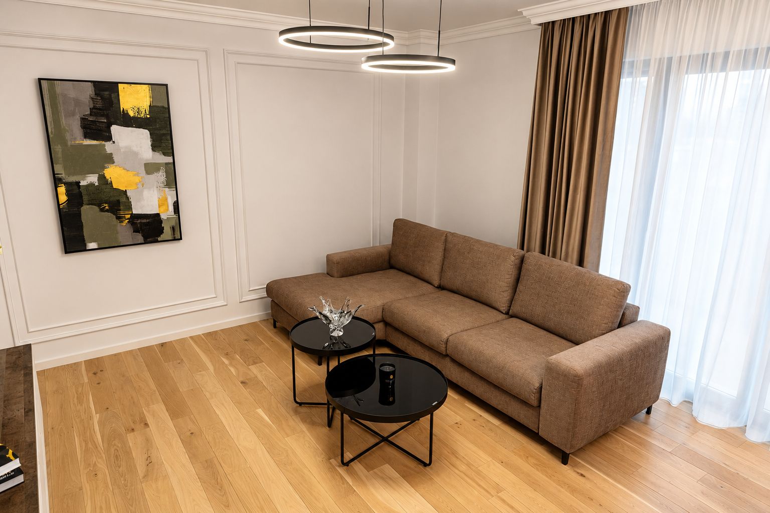 Una sala de estar moderna con un sofá modular, dos mesas redondas negras y un cuadro abstracto contemporáneo en la pared.