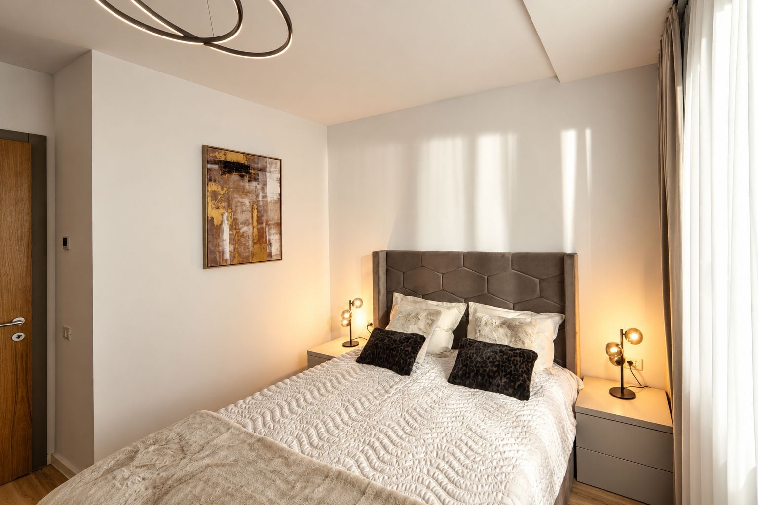 Une chambre à coucher avec un grand lit, une tête de lit ornée d’un motif géométrique, deux lampes de chevet et un tableau accroché au mur.