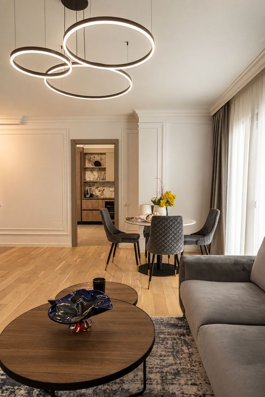 Un salon moderne avec une table basse ronde, un canapé gris et un coin repas comprenant une table et des chaises.