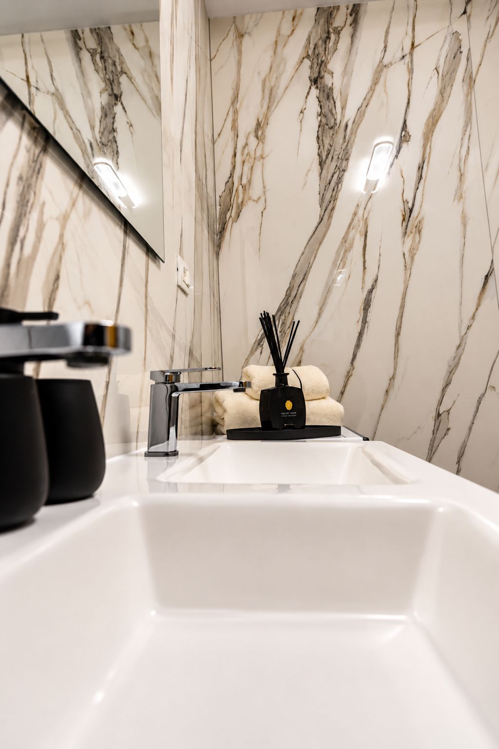 Un bany amb un lavabo blanc, un mirall i una paret de marbre.