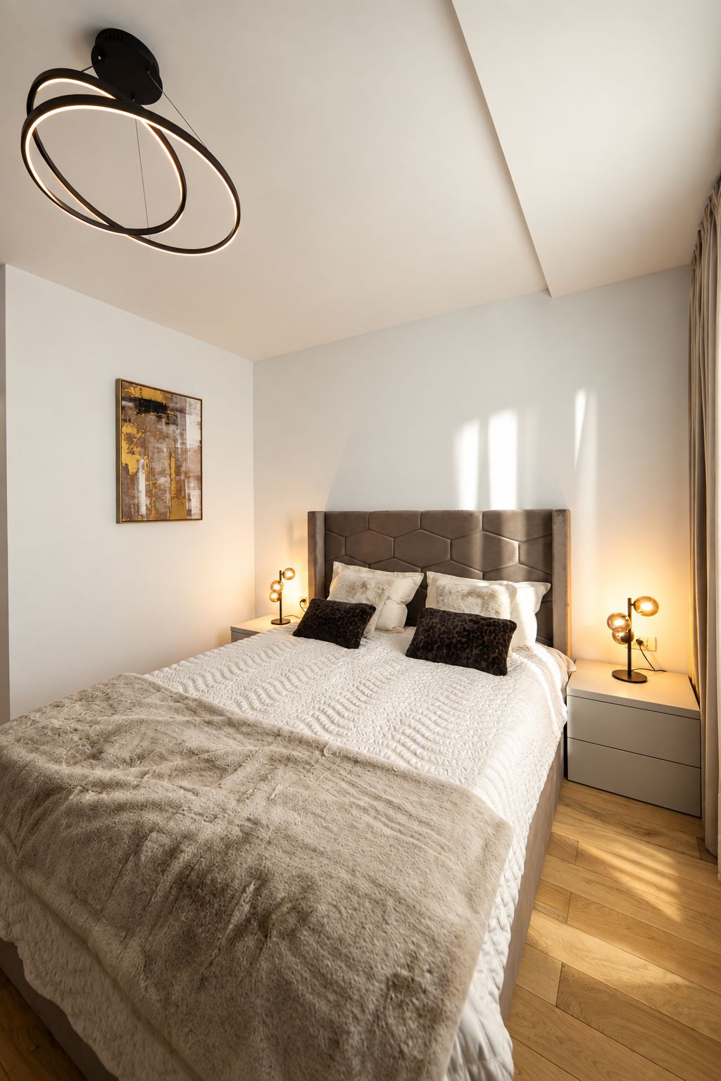 A modern bedroom with a large bed, a headboard with hexagonal panels, two bedside lamps, and a ceiling light fixture.