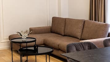 A modern living room with a brown sectional sofa, two black round tables, and a dining table with chairs.