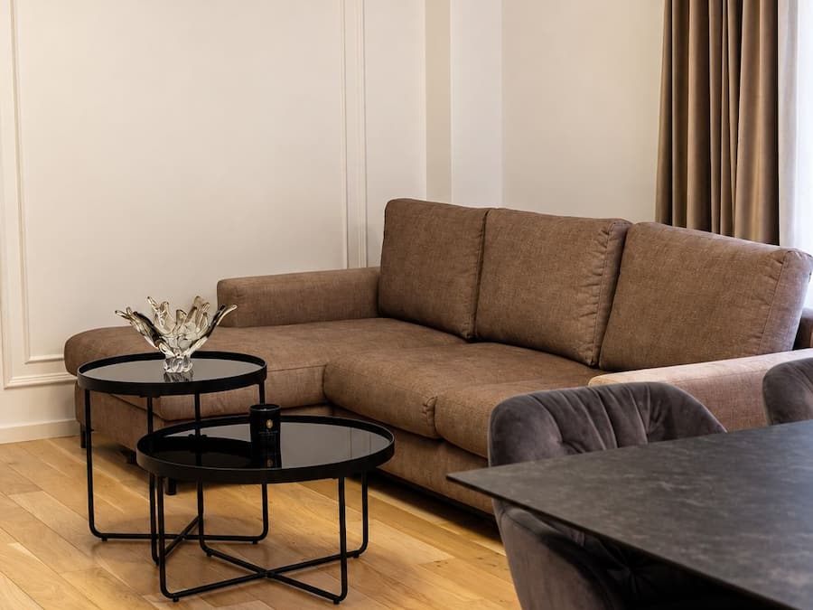 En moderne stue med en brun hjørnesofa, to sorte runde borde og et spisebord med stole.