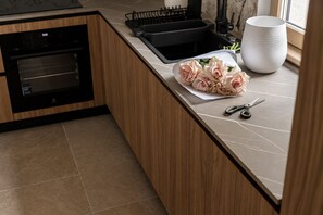 A kitchen with a built-in oven, a sink, and a countertop with a bouquet of flowers and a pair of scissors. - MaisonA (Timișoara)