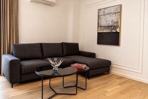 Una sala moderna con un sofá gris oscuro, una mesa de centro negra redonda con un objeto de vidrio decorativo y un cuadro abstracto enmarcado en la pared.