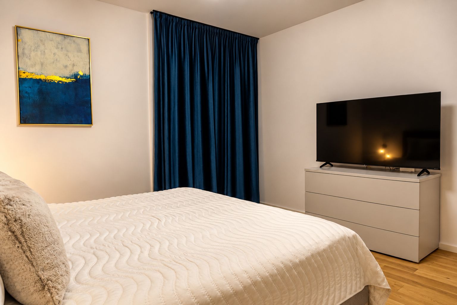 Un dormitorio con una cama, un televisor en una cómoda, un cuadro en la pared y una cortina azul.