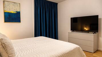Un dormitorio con una cama, un televisor en una cómoda, un cuadro en la pared y una cortina azul.