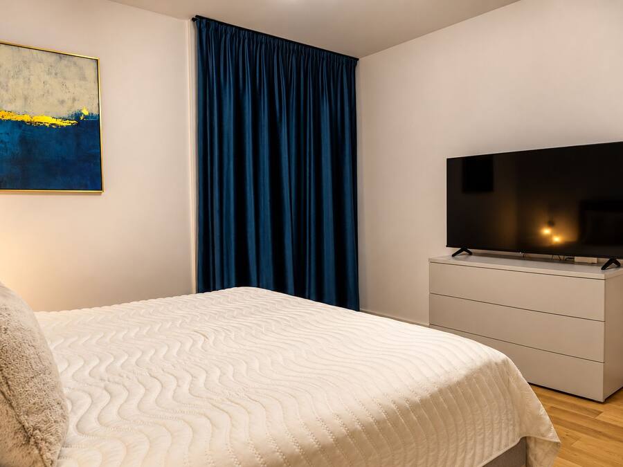 Un dormitorio con una cama, un televisor en una cómoda, un cuadro en la pared y una cortina azul.