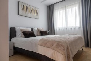 Une chambre à coucher comprenant un lit, une table de chevet, une œuvre d’art accrochée au mur et une fenêtre avec des rideaux.