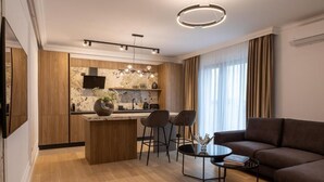 A modern kitchen with a central island, bar stools, a round coffee table, and a dark-colored sofa in a living area. - MaisonA (Timișoara)