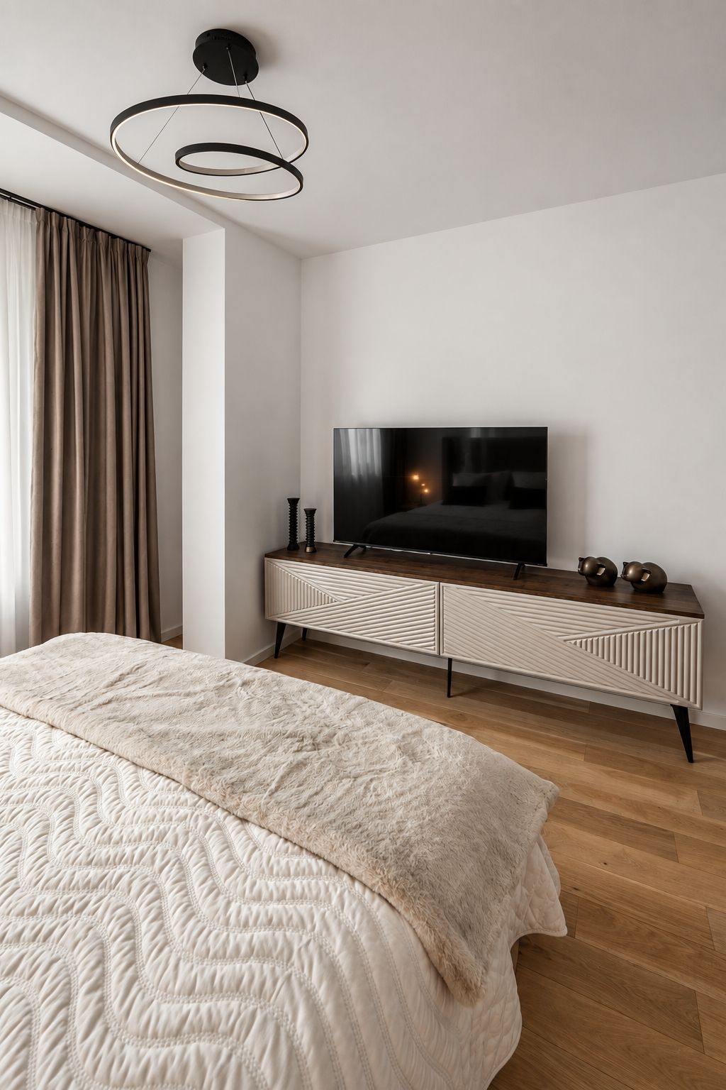 A modern bedroom with a large bed, a television on a wooden dresser, and a ceiling light fixture.