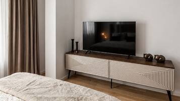 A modern bedroom with a large bed, a television on a wooden dresser, and a ceiling light fixture.