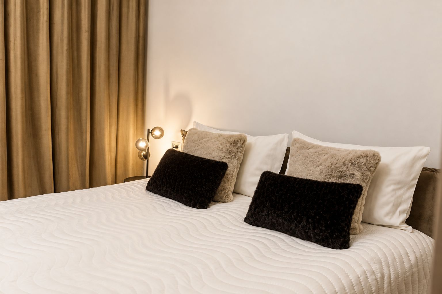 A neatly made bed with a white quilt, two fluffy pillows, and a bedside lamp.