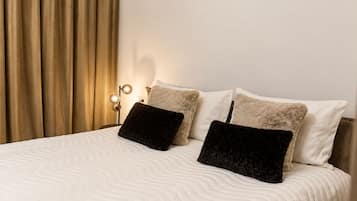 A neatly made bed with a white quilt, two fluffy pillows, and a bedside lamp.
