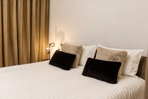 A neatly made bed with a white quilt, two fluffy pillows, and a bedside lamp. - MaisonA (Timișoara)