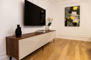 A modern living room with a wooden console table, a flat-screen TV, and a painting on the wall.