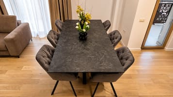 A dining table with a dark surface and six upholstered chairs, a vase with flowers, and a wooden floor.