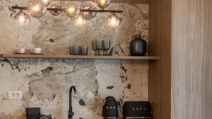A modern kitchen with a marble backsplash, wooden cabinets, a black countertop, and a pendant light fixture. - MaisonA (Timișoara)