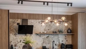 A modern kitchen with a marble backsplash, wooden cabinets, a central island with bar stools, and pendant lighting. - MaisonA (Timișoara)