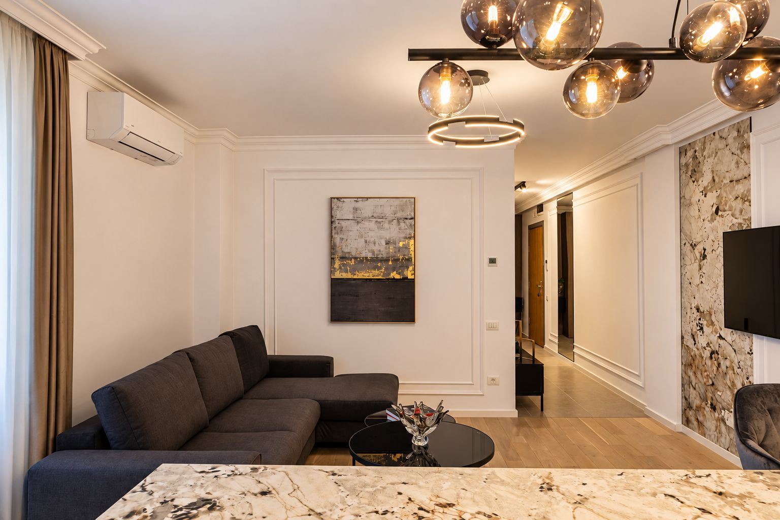A modern living room with a sectional sofa, a marble coffee table, and a unique spherical light fixture.