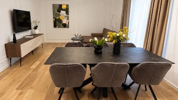 A modern dining area with a rectangular table, four chairs, a flat-screen TV, a console table with a vase, and a painting on the wall.