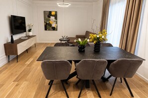 A modern dining area with a rectangular table, four chairs, a flat-screen TV, a console table with a vase, and a painting on the wall. - MaisonA (Timișoara)